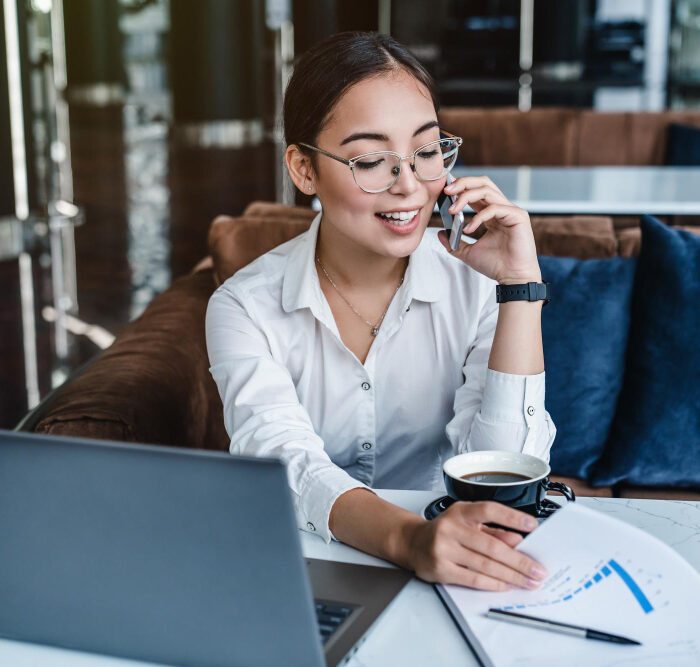 Asian businesswoman talking on the phone while sitting at a table, discussing website cost options for 2024.