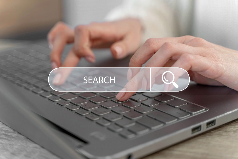 Close-up of hands typing on a laptop keyboard with a transparent "SEARCH" bar overlaid on the image, perfect for a small business owner researching effective marketing strategies.