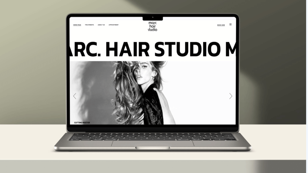 A laptop on a desk displaying the homepage of a hair studio website with monochromatic web design featuring an image of a model with flowing hair.