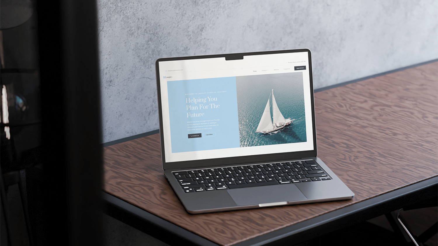 Laptop on a wooden desk displaying a web design for a financial planning website with an image of a sailboat on the screen.